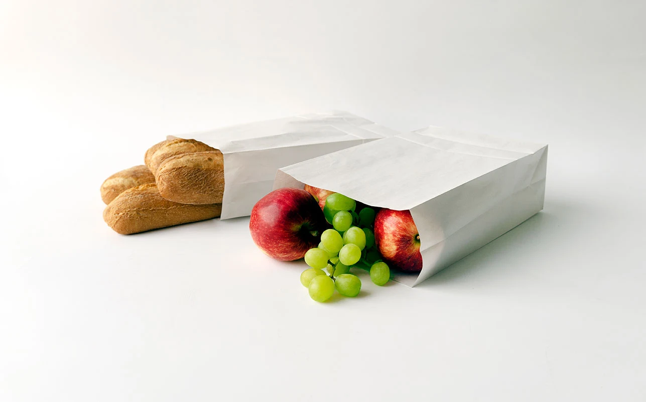 Bröd och frukt i vita papperspåsar