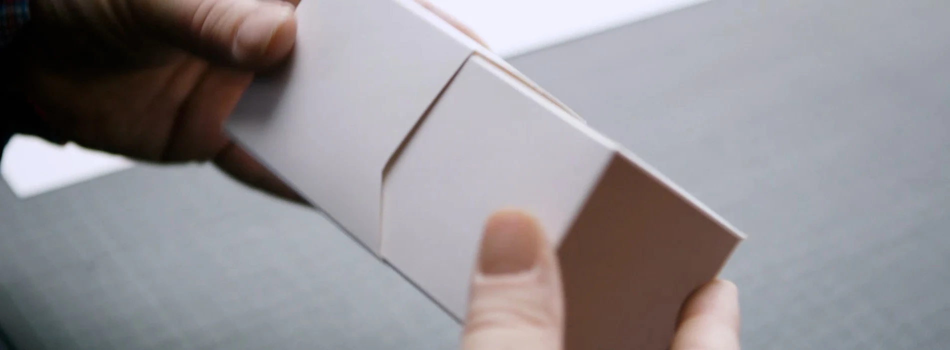 A pair of hands holding a plain white paperboard mock-up packaging