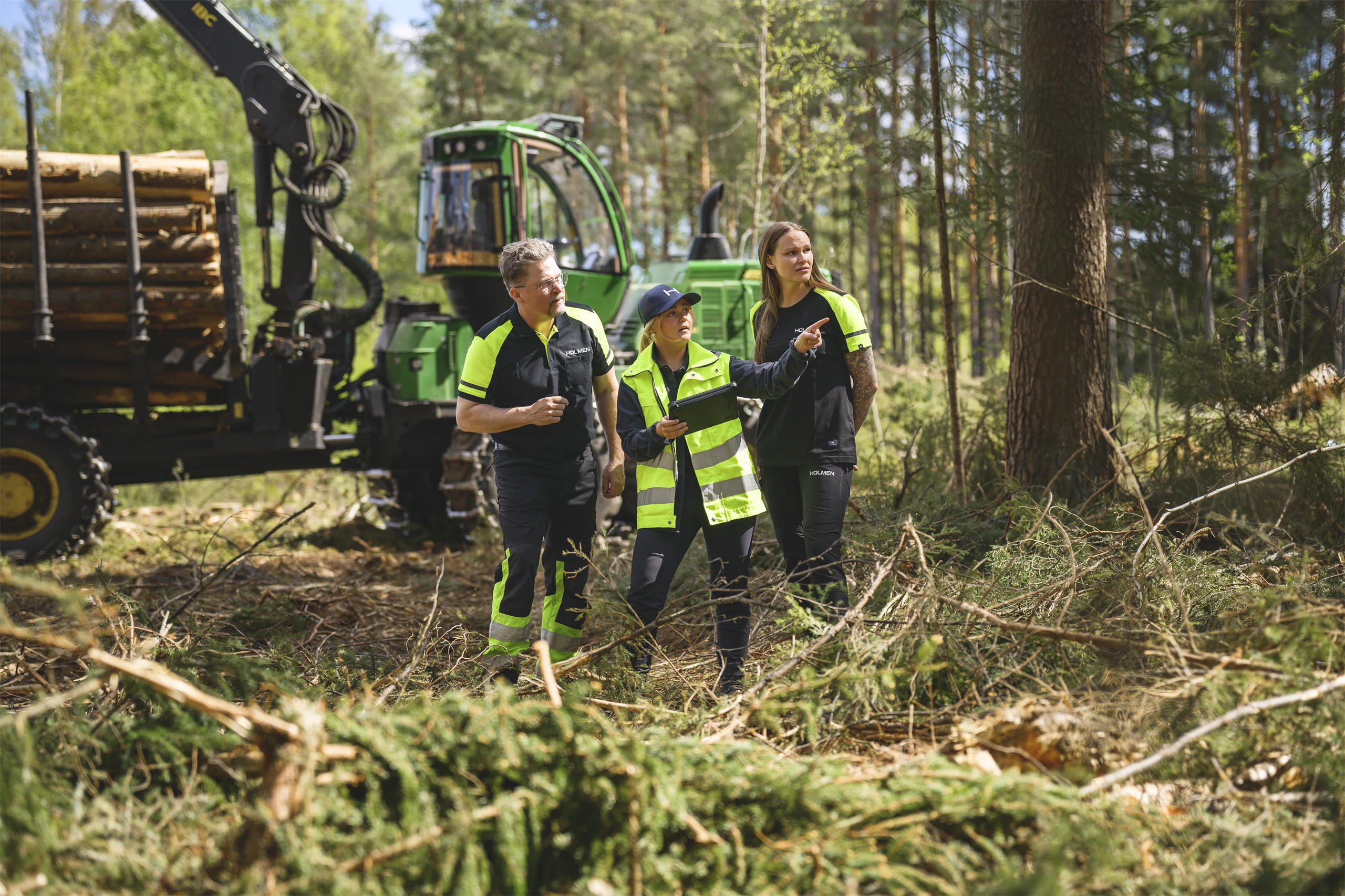 Three engaged Holmen employees discussing in front of a forestry machine – focusing on employeeship, collaboration and responsibility.