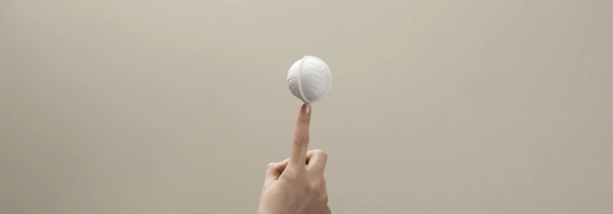 White wood-based packaging in the shape of a ball, balancing on a fingertip