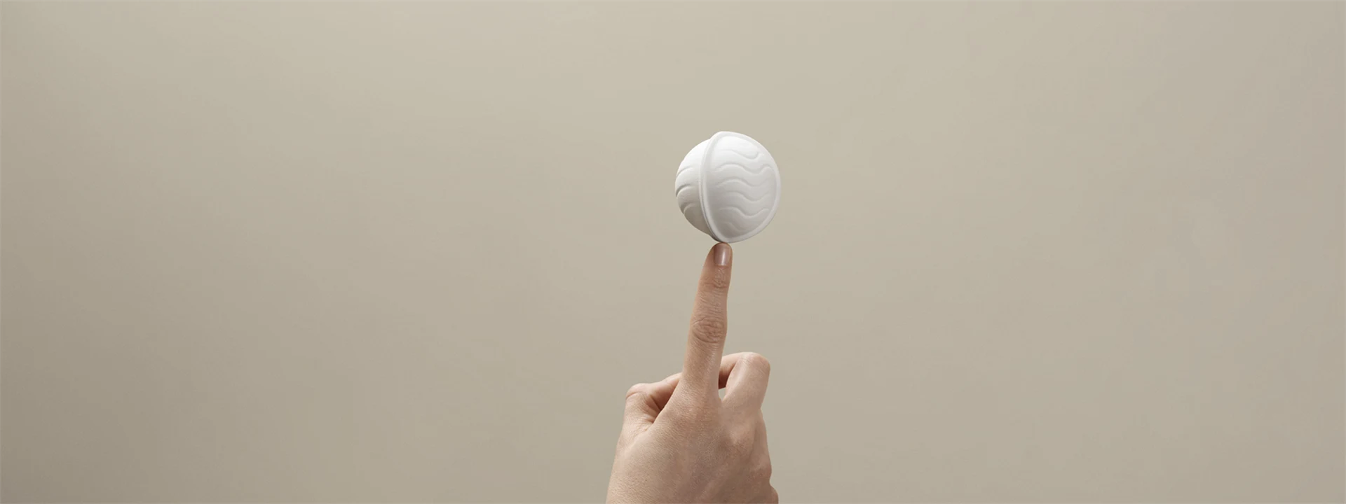White wood-based packaging in the shape of a ball, balancing on a fingertip