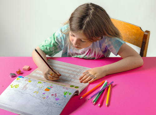 Girl writing in workbook at school, handwriting stimulates learning