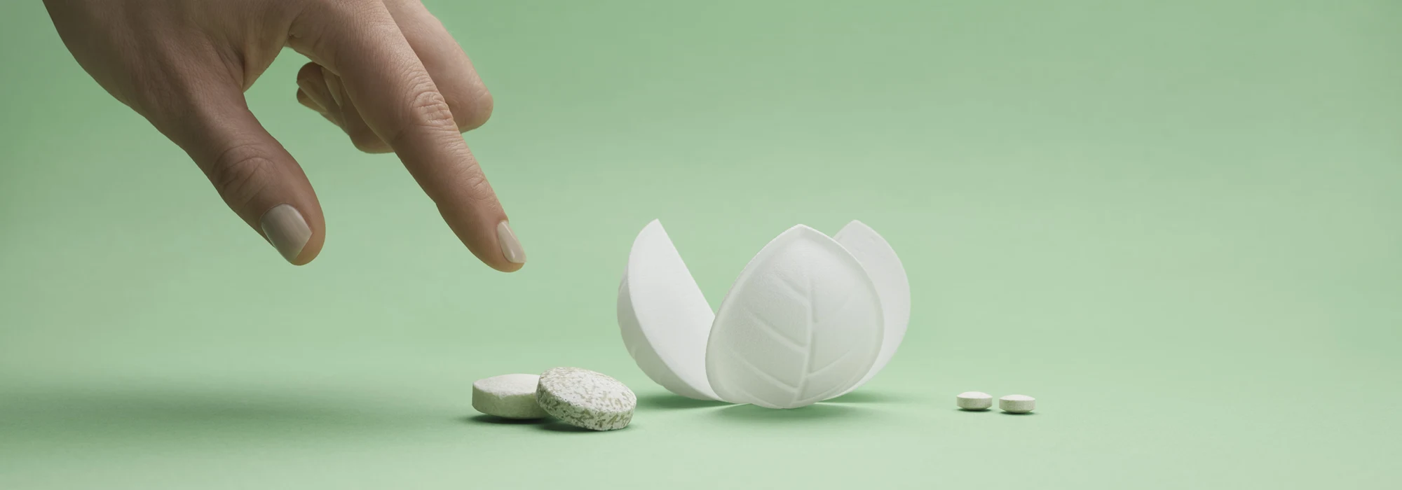 FIngers pointing at dissolvable tablets and a flower-like piece of packaging on green background