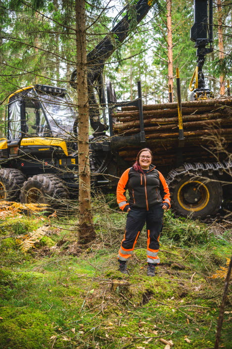 Kvinnlig skoterförare står stolt framför framför maskinen i skogen.