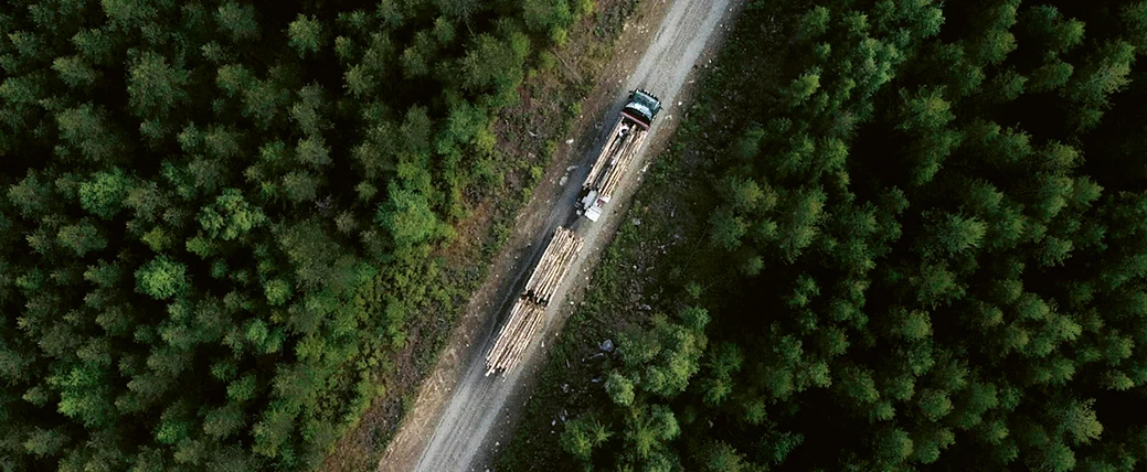 Drönarbild på timmerbil på väg genom skogslandskap