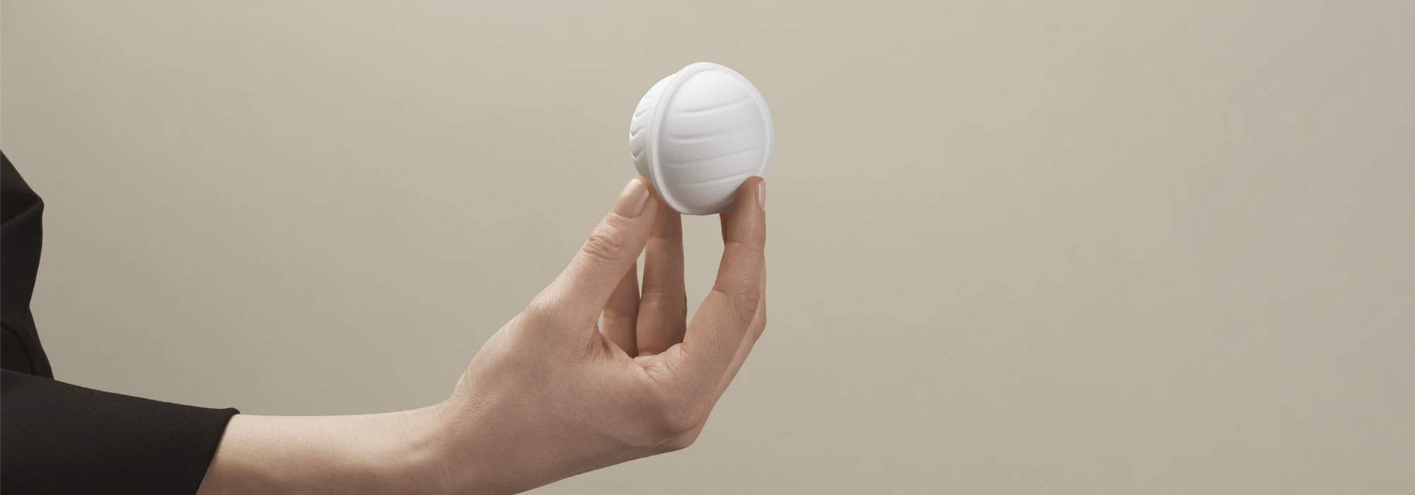 Hand holding a piece of wood-based packaging in the shape of a ball