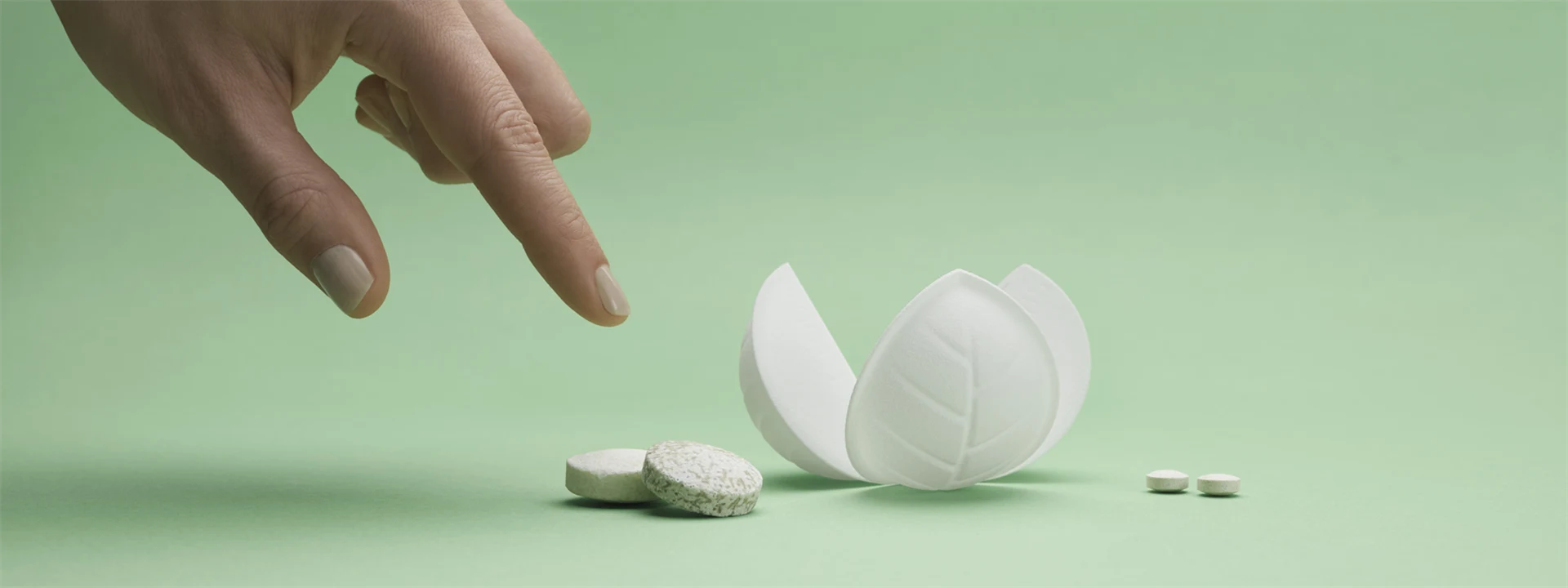 FIngers pointing at dissolvable tablets and a flower-like piece of packaging on green background