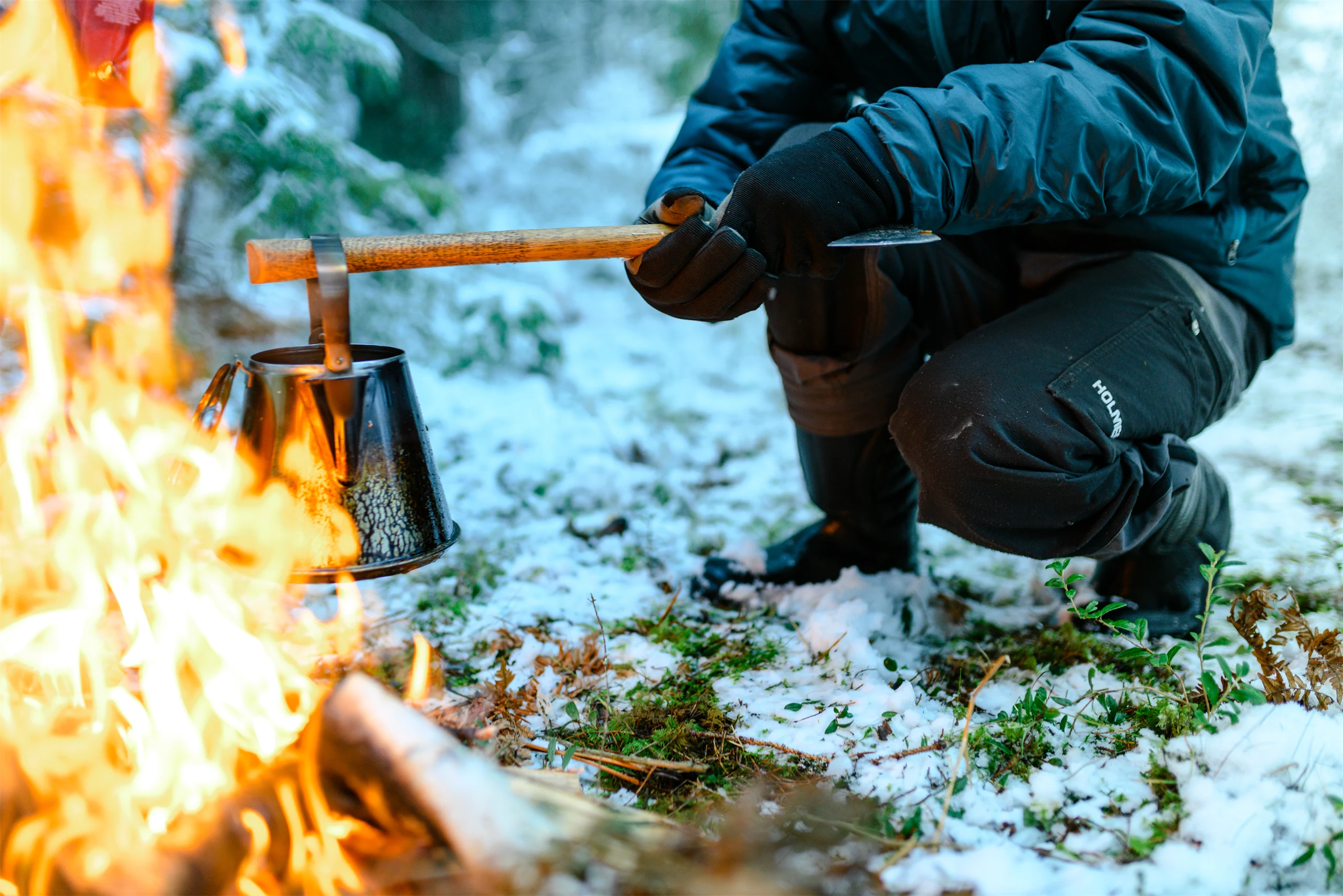 Bild på man som värmer en kanna över öppen eld i skogen