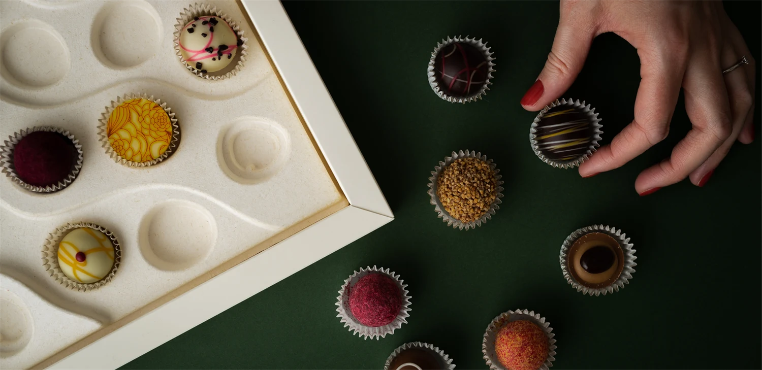 Chocolate pralines spread out around a paperboard packaging